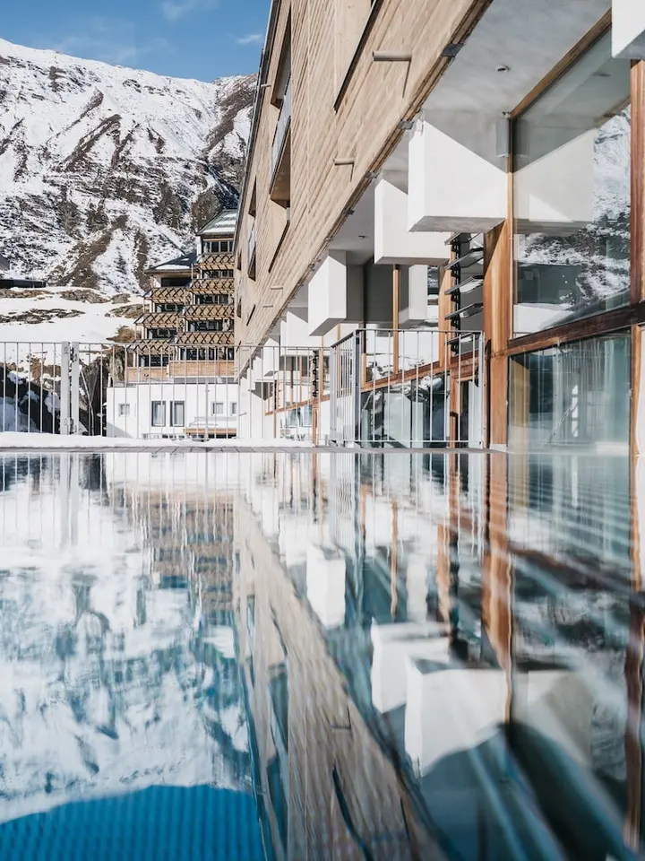 The Crystal Vaya Unique in Obergurgl, its glass-fronted facade reflected in the water outside