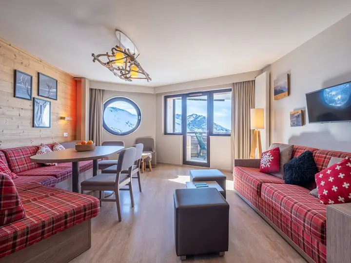 Living room of a two-bedroom apartment at Pierre & Vacances Residence Atria-Crozats, with a round window onto the mountains